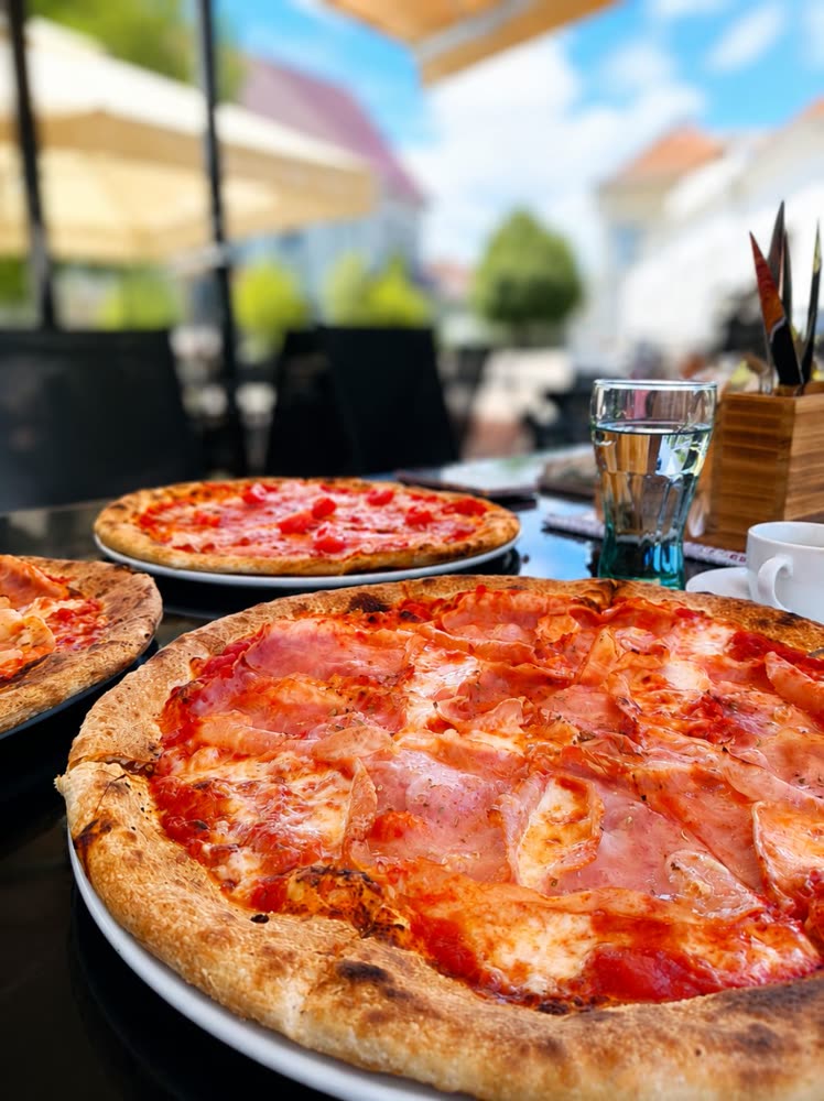 Sonkás pizza közelről, terasz és kék ég a háttérben